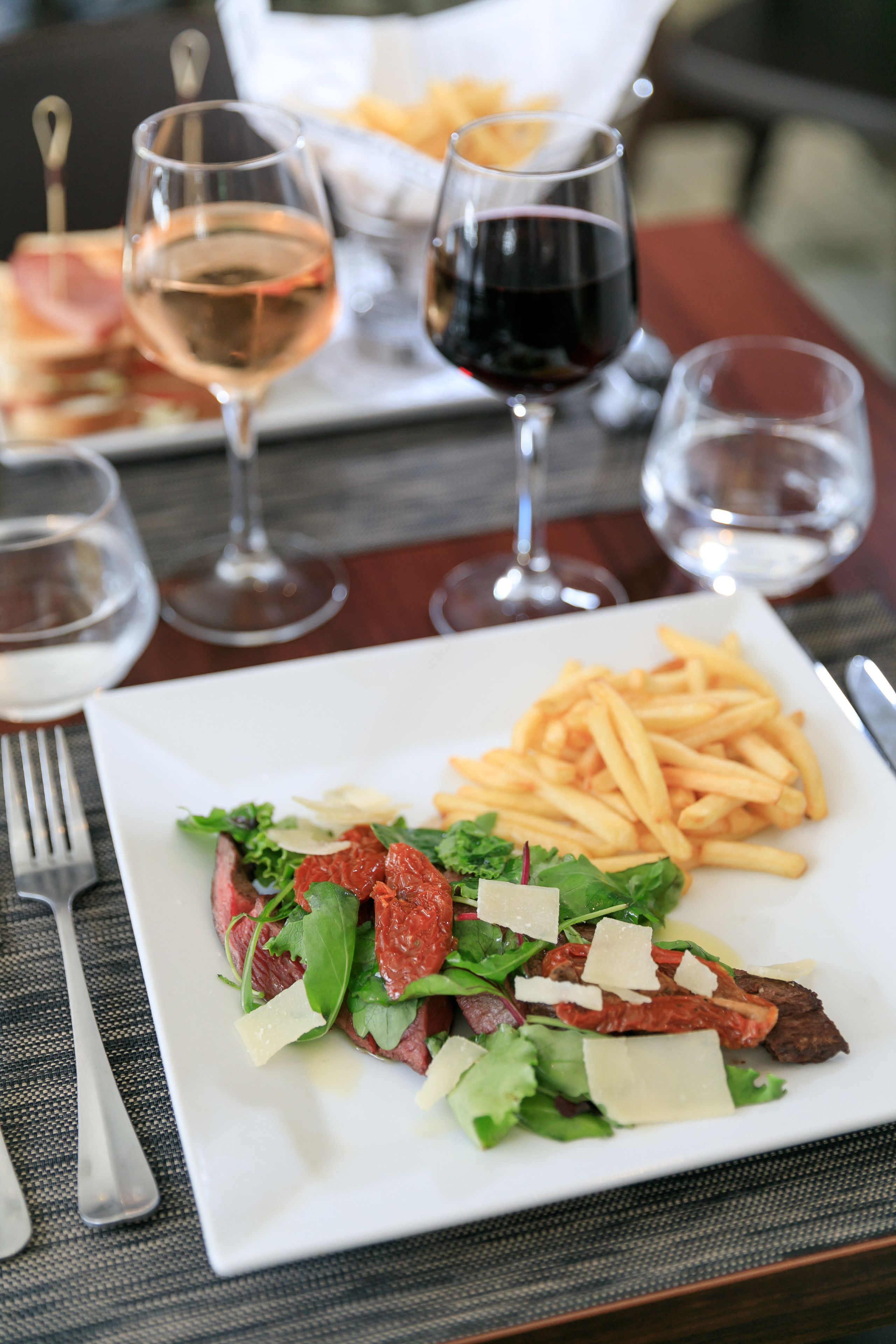 A dining table with a plate of steak and fries, wine glasses, and cutlery.