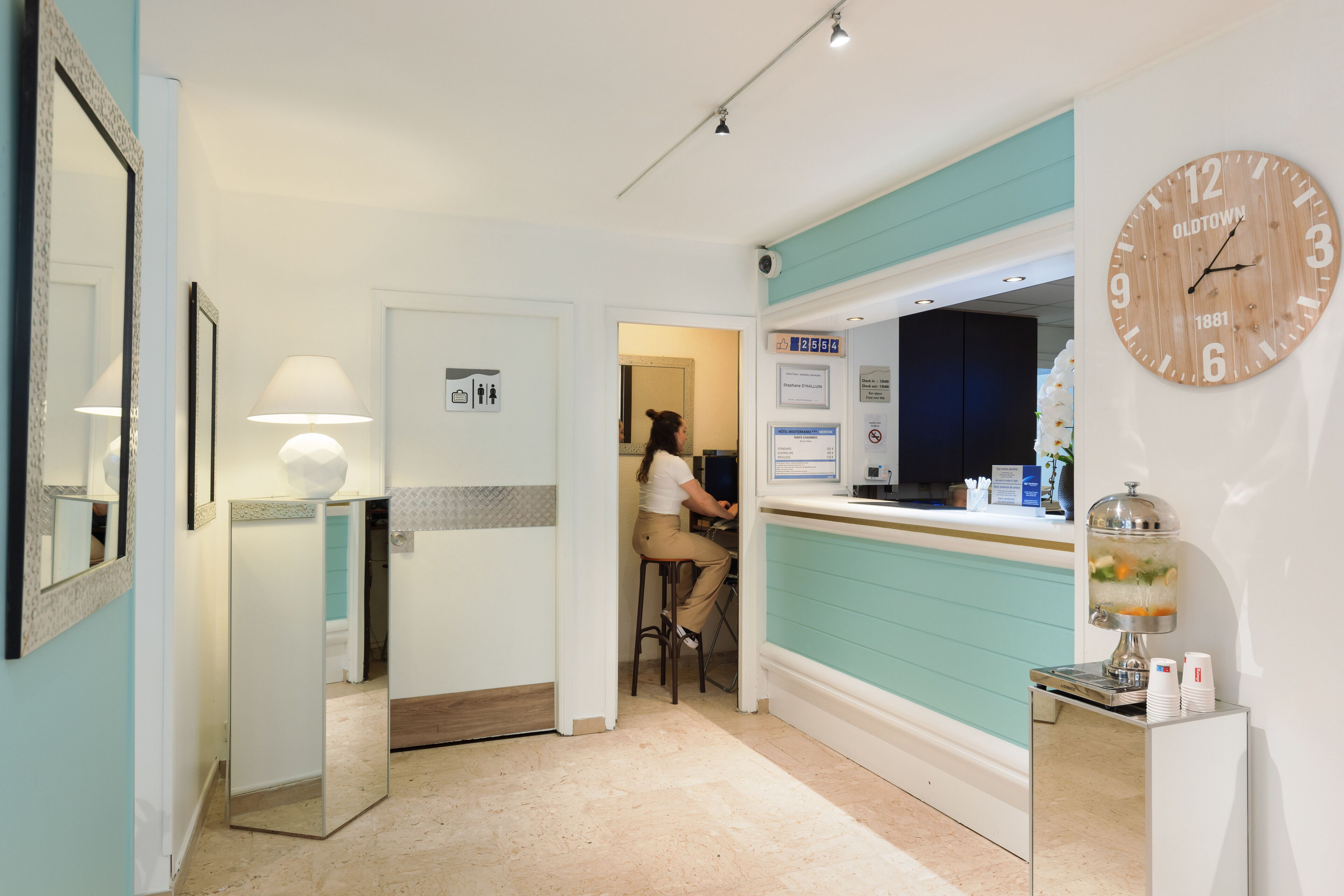 A hotel lobby with a reception desk, a clock, and a wall-mounted sign.