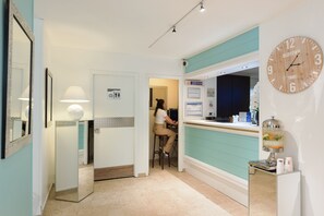 Un vestíbulo de hotel con mostrador de recepción, un reloj y un letrero en la pared.