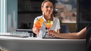 A bar area with a counter, glasses of cocktails, and a view of the city through a window. - Best Western Hotel Mediterranee Menton (Menton)