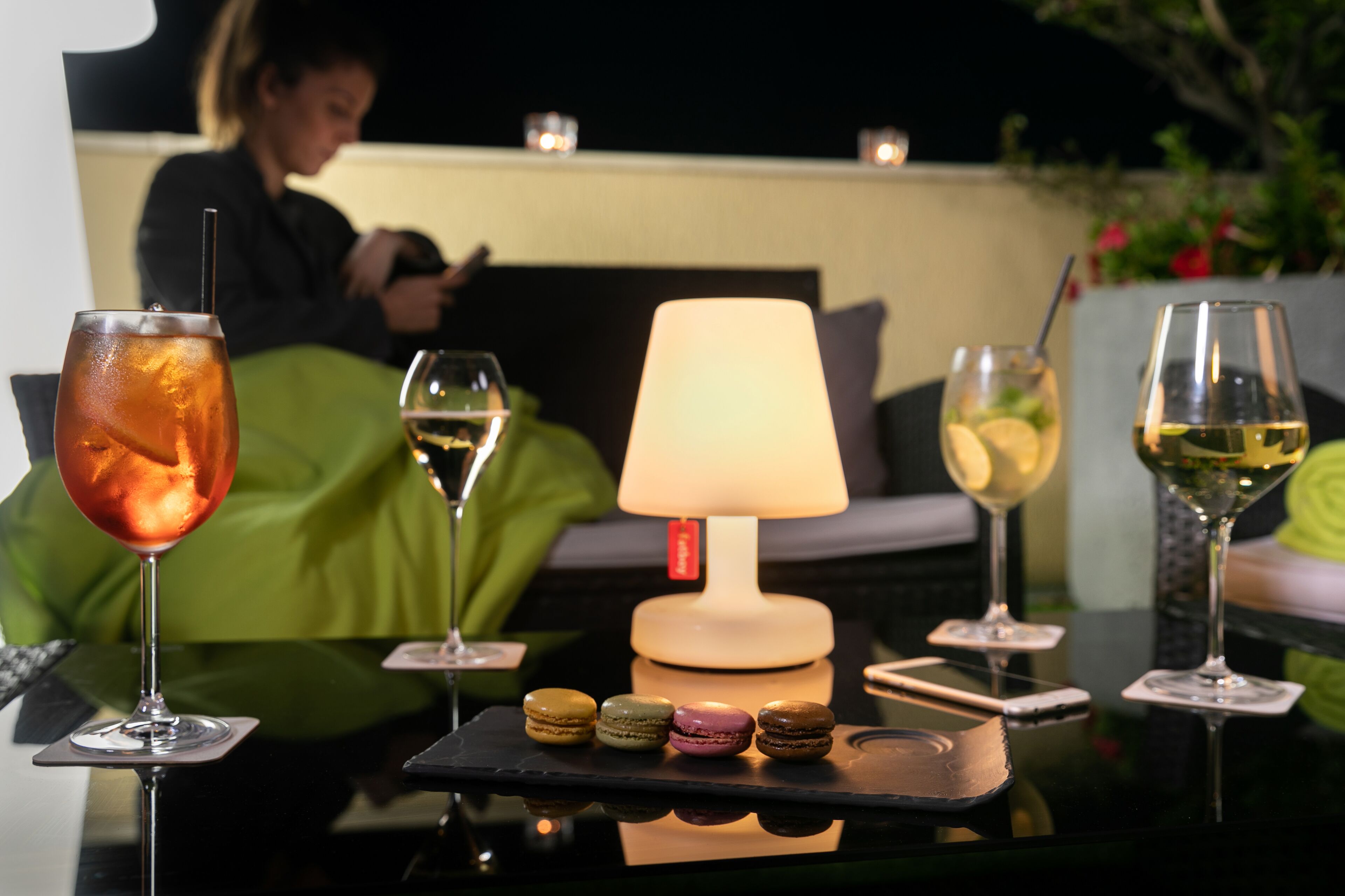 Una mesa con bebidas, una lámpara y macarons.