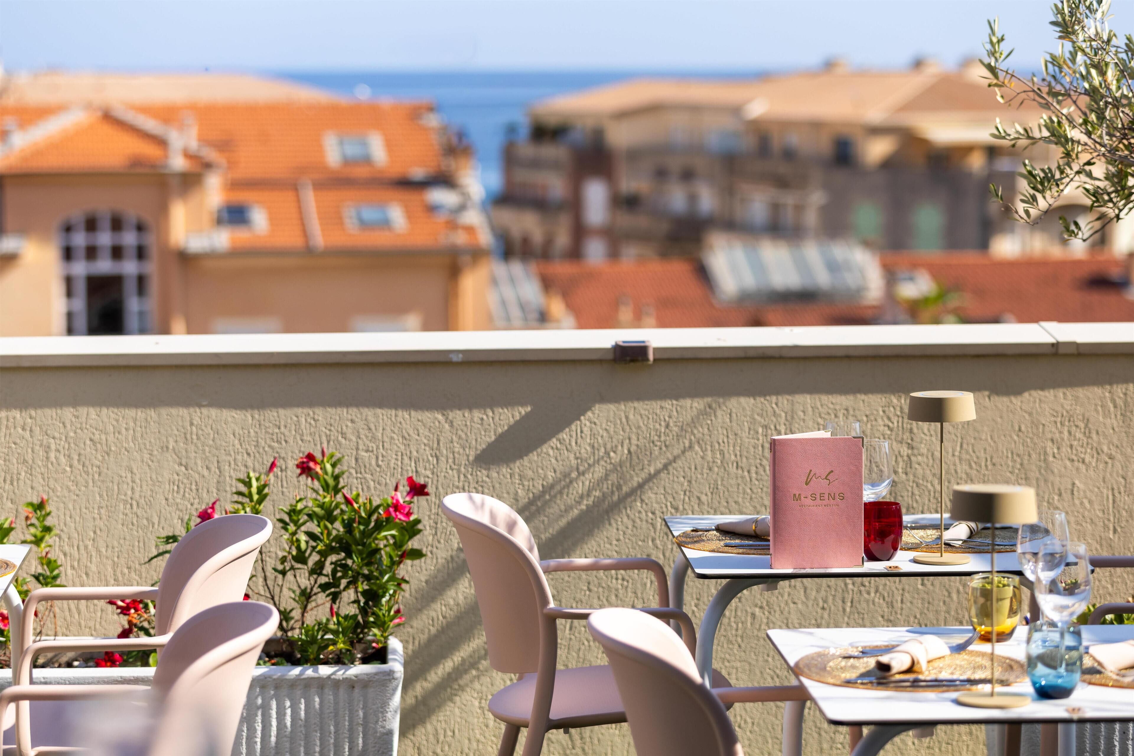 Une terrasse avec des places assises extérieures, un menu et une vue sur les bâtiments et la mer.