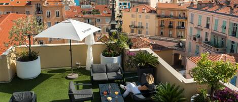 Une terrasse sur le toit, dotée d’un espace extérieur aménagé avec des sièges, d’un grand parasol et de plantes en pot.