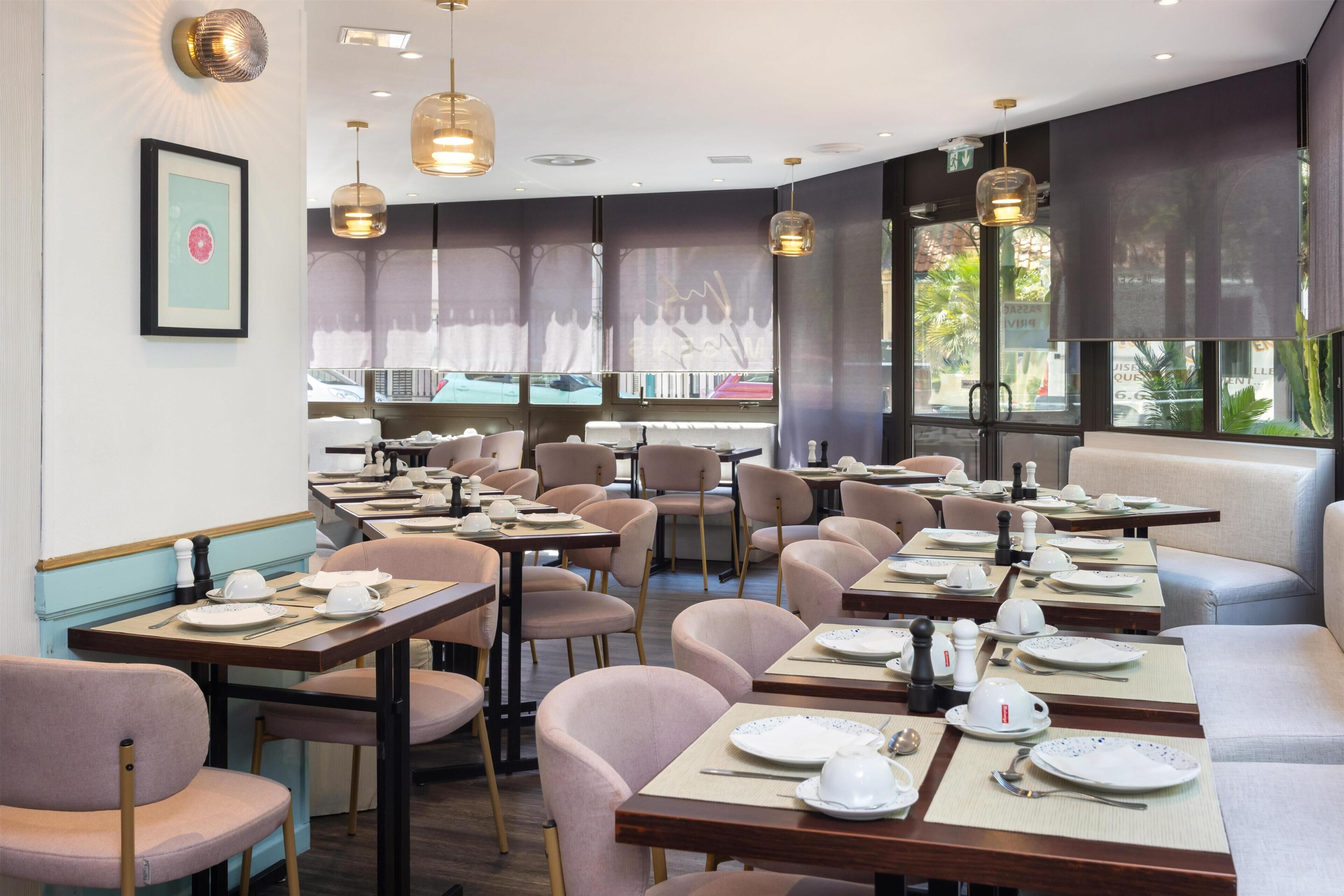 Un restaurant avec des tables dressées pour le service, des chaises et des lampes suspendues.