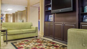 A lobby with a green sofa, a flat-screen TV mounted on a wooden cabinet, and a patterned rug.