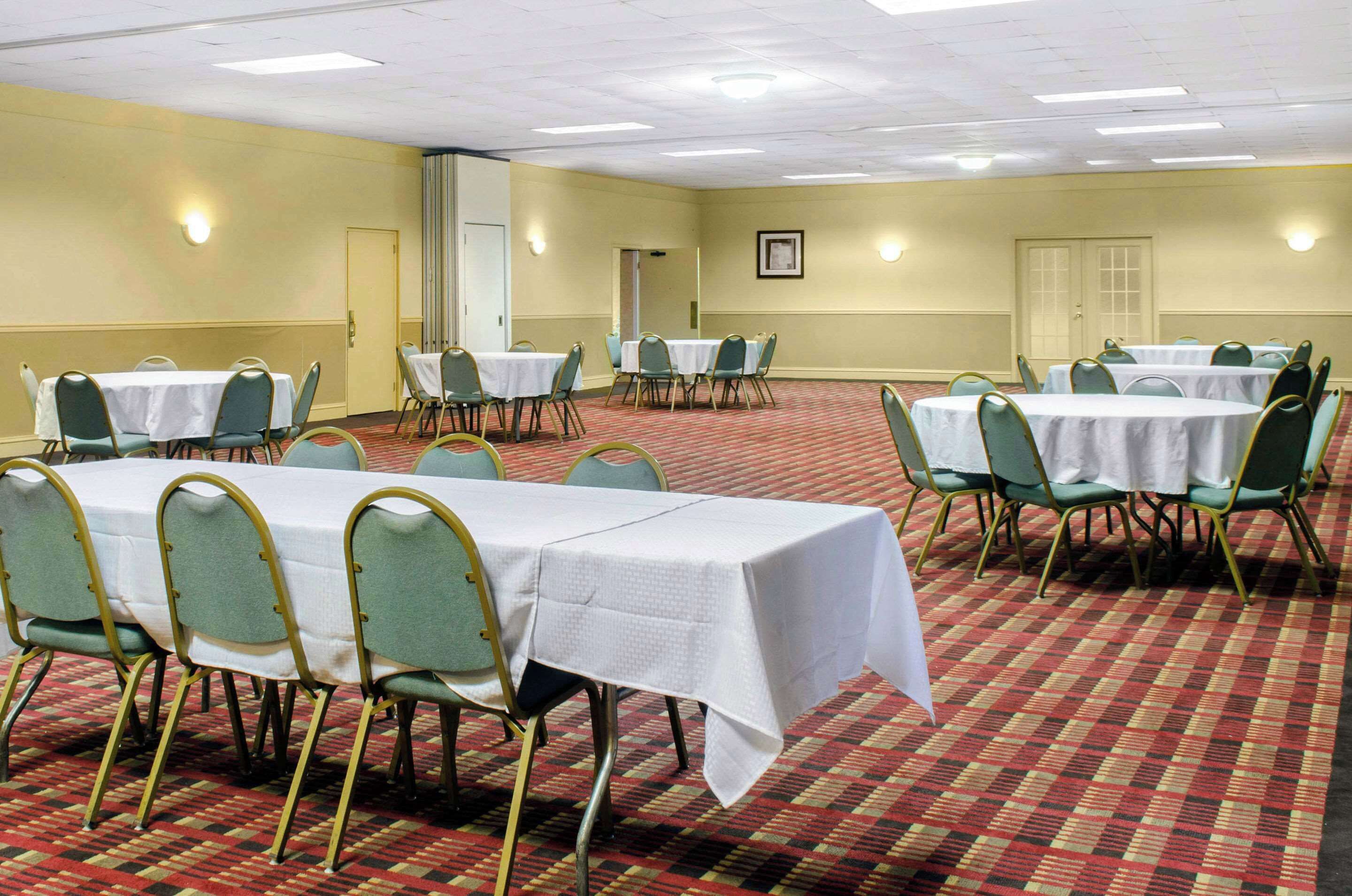 A conference room with multiple tables and chairs, carpeted floor, and walls with light fixtures.