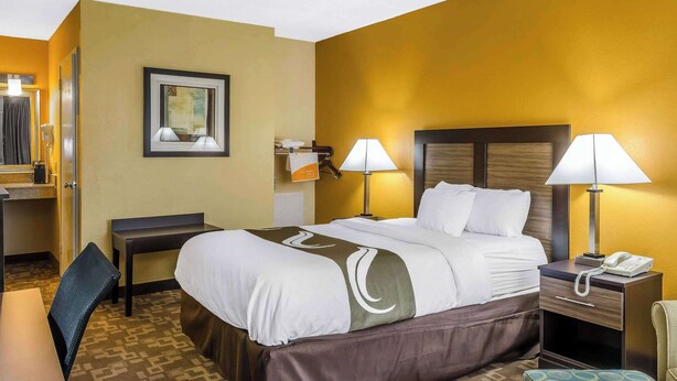 A hotel room with a bed, bedside tables, a desk, and a chair.