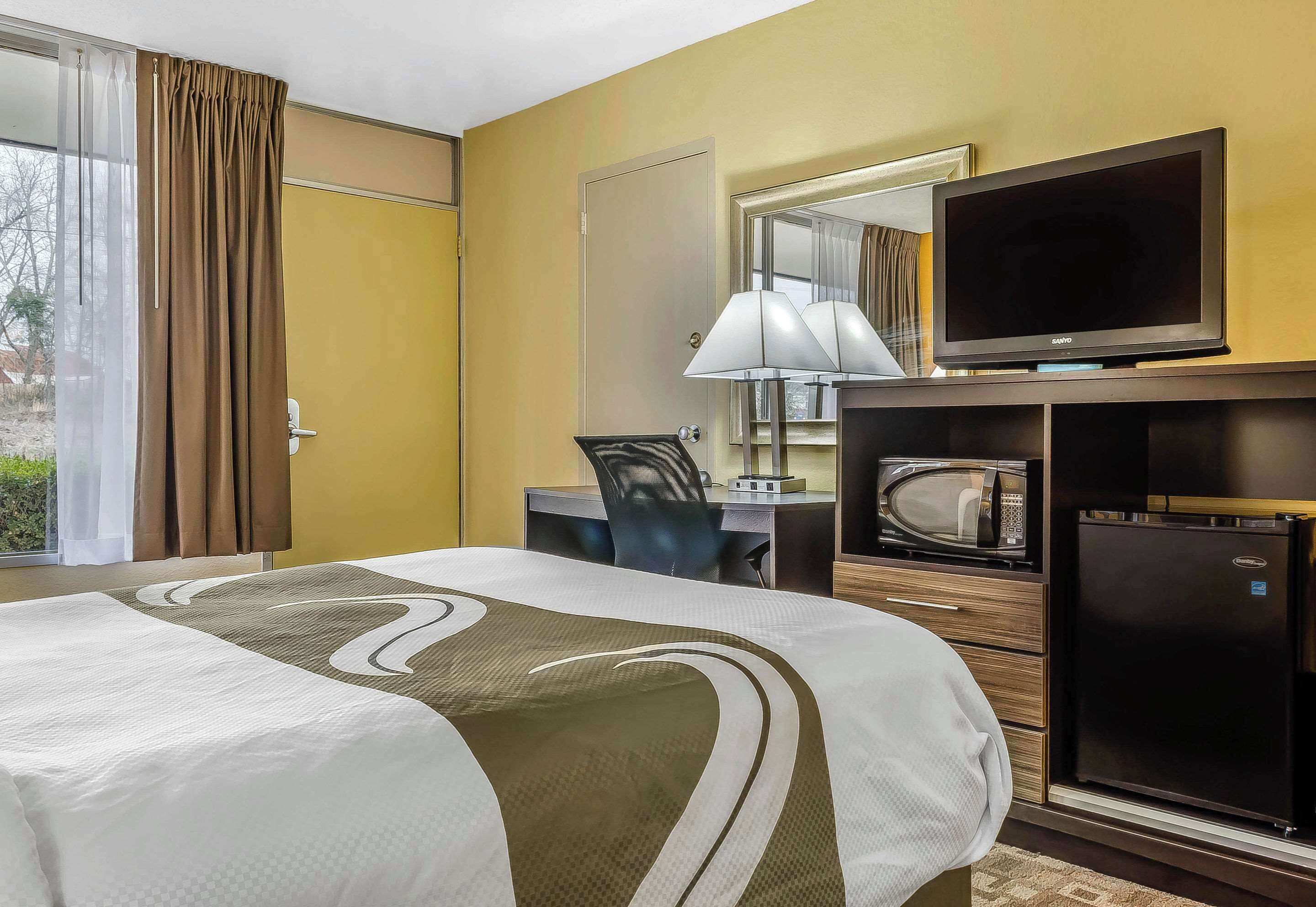 Habitación de hotel con cama, escritorio, silla, televisor, microondas y refrigerador.