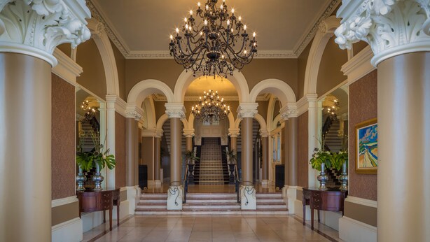 A grand hallway with a chandelier, columns, and a staircase leading to an upper floor. - The Royal Marine Hotel (Dublin)