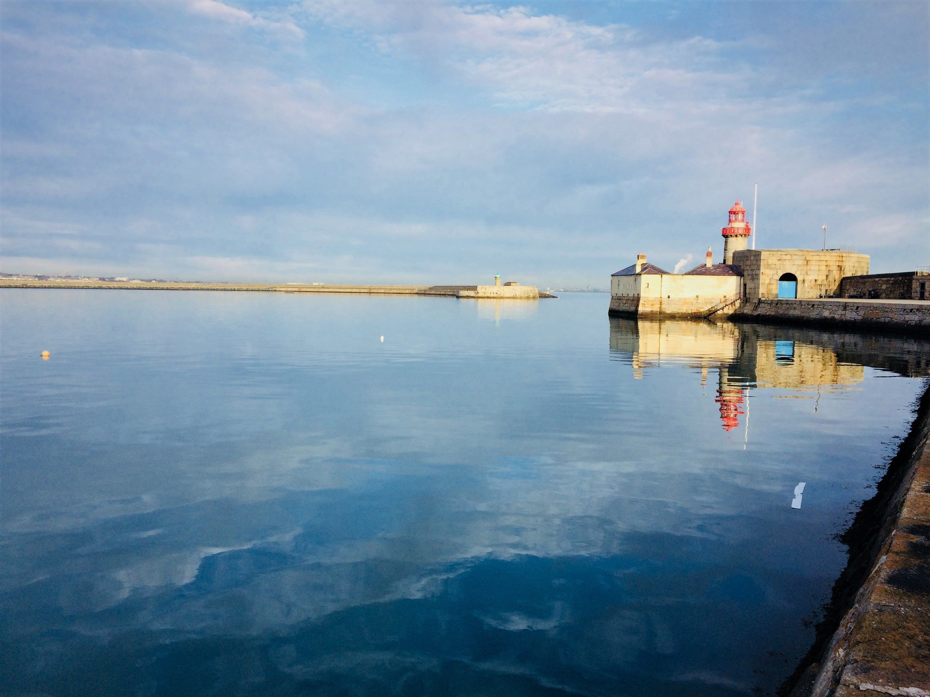 Una orilla tranquila con un faro y un muelle de piedra que se adentra en el agua.