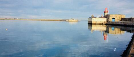 Una orilla tranquila con un faro y un muelle de piedra que se adentra en el agua.
