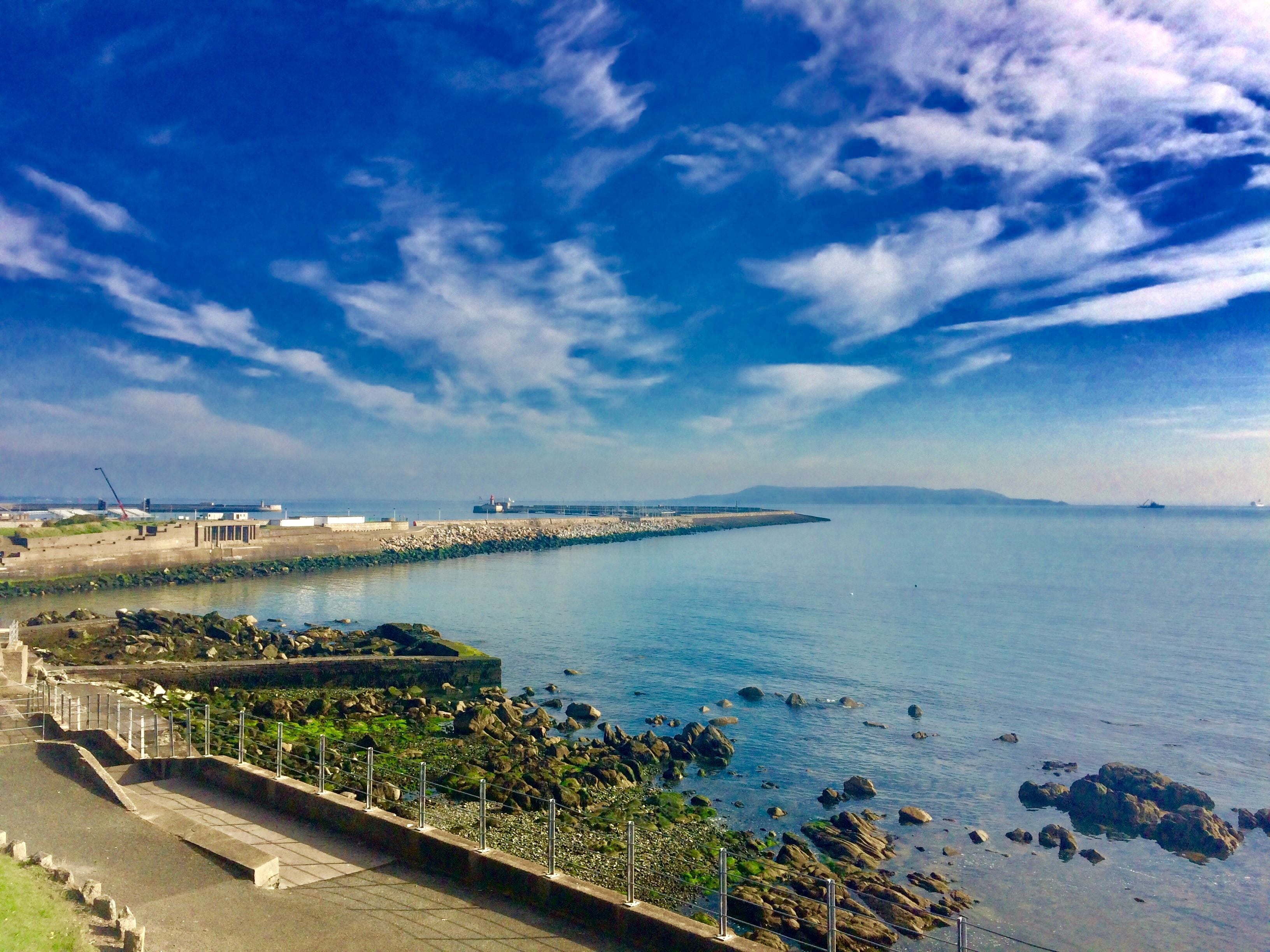 A coastal view with a rocky shoreline, a pier, and a distant ship.