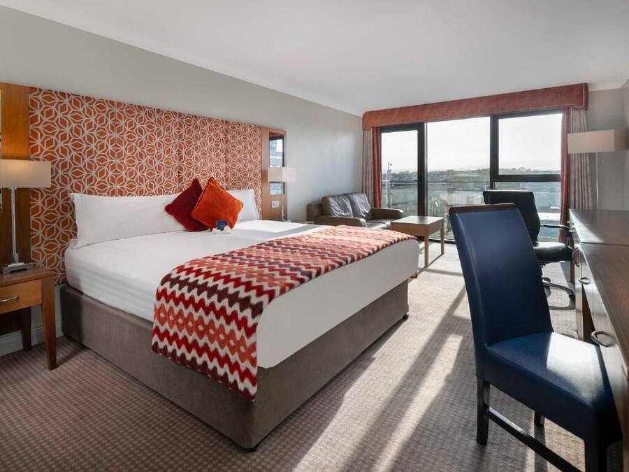 A hotel room with a large bed, a desk, a chair, and a view of the city.