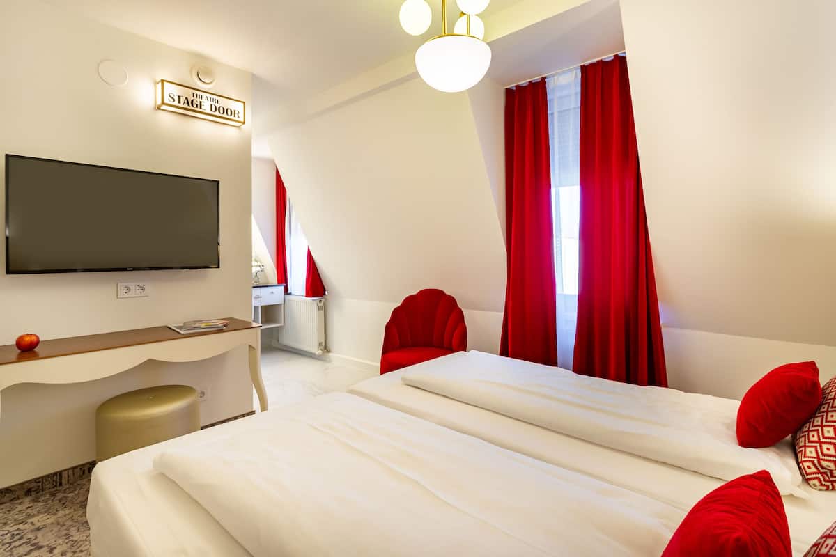A hotel room with a bed, a desk, a television, and red curtains.