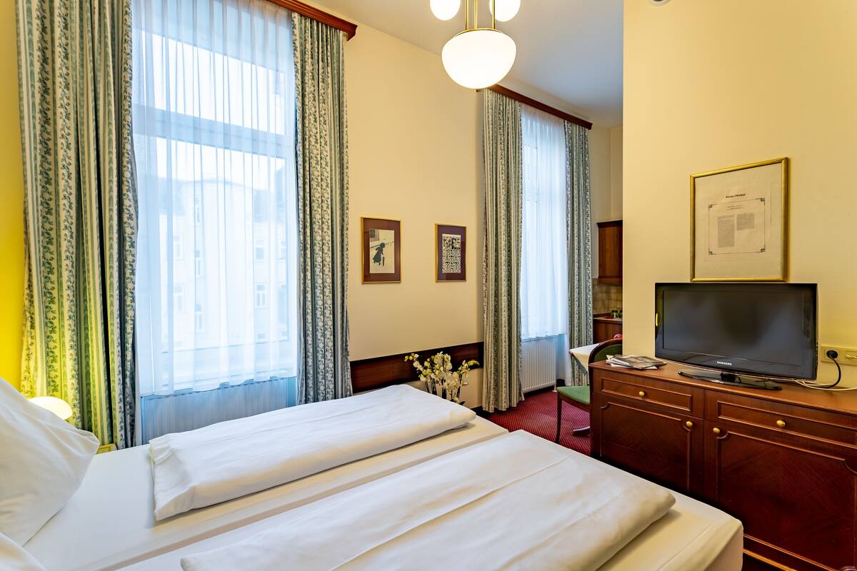 A hotel room with two beds, a television on a wooden dresser, and a framed certificate on the wall.