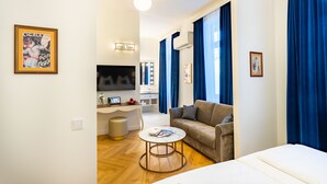 Una sala de estar moderna con un sofá, una mesa de centro y un televisor. Se ve un área de cocina al fondo con cortinas azules.