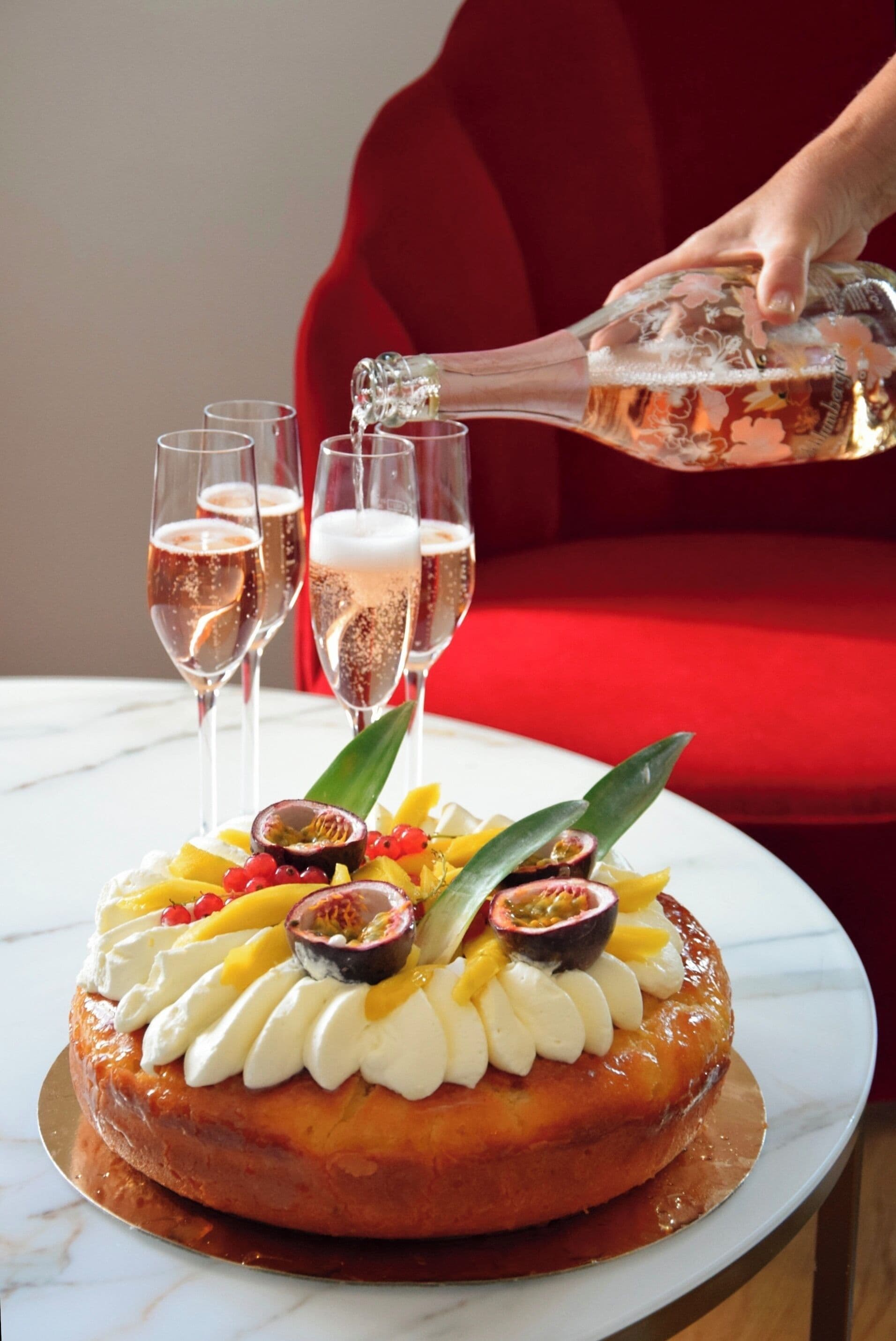 Un postre con fruta y crema batida, una botella siendo servida en vasos, y una silla roja al fondo.