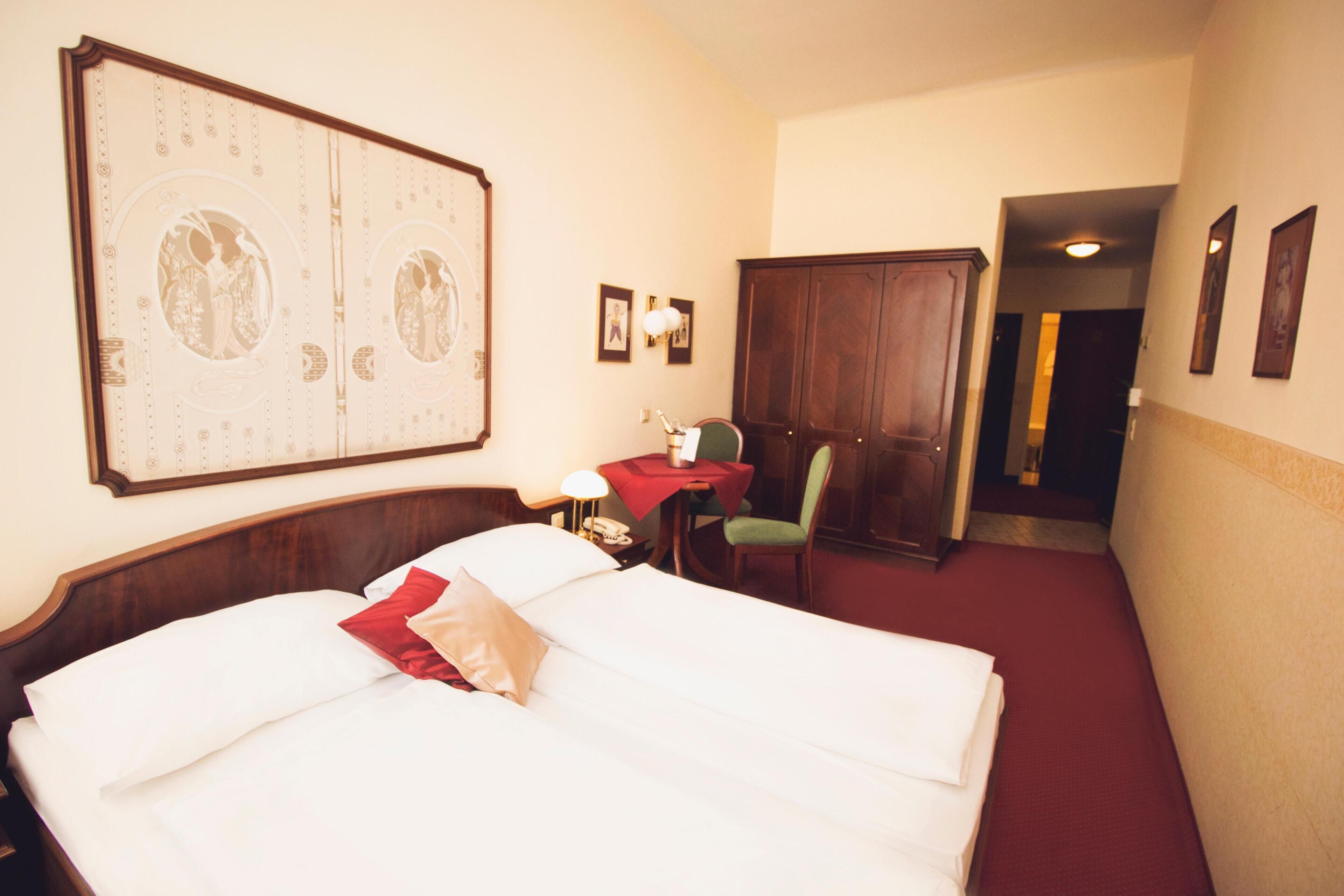 A hotel room with a large bed, a desk, a chair, a wardrobe, and a wall-mounted artwork.