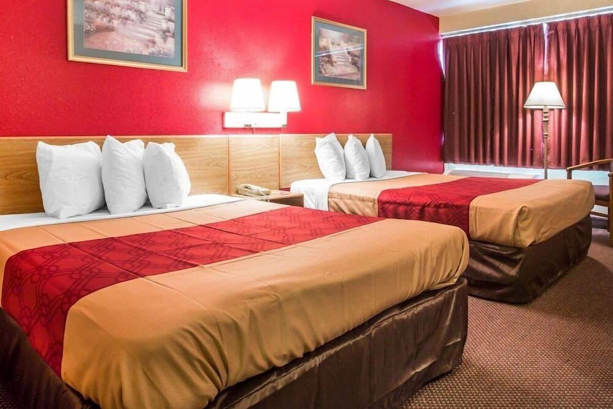 A hotel room with two beds, red walls, and two framed pictures.