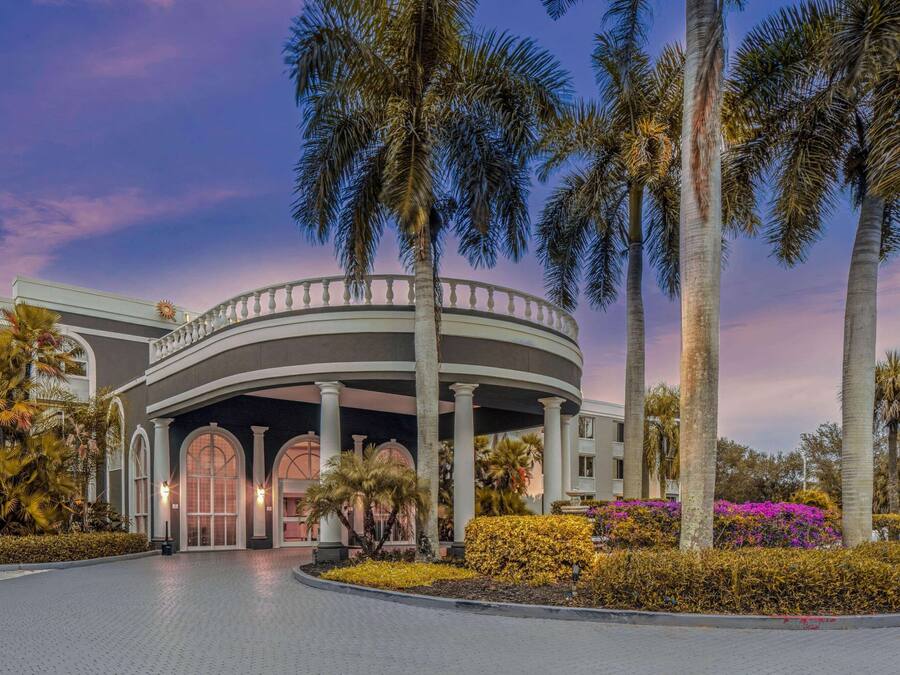 A hotel entrance with a circular colonnade, palm trees, and well-maintained landscaping.
