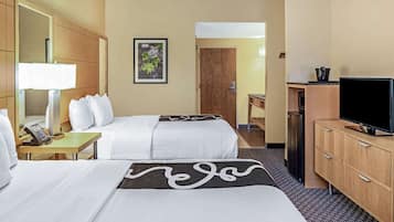 Quarto de hotel com duas camas, uma escrivaninha com candeeiro, televisão e um armário de madeira.