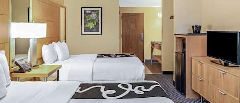 Ein Hotelzimmer mit zwei Betten, einem Schreibtisch mit Lampe, einem Fernseher und einem Holzkasten.