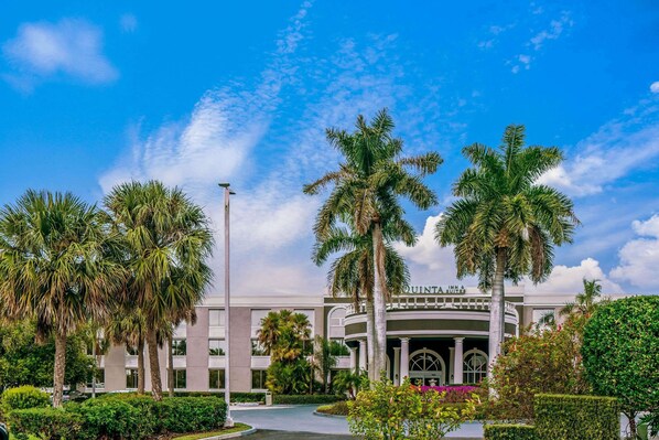 A hotel with a modern facade, palm trees, and a clear blue sky. - La Quinta Inn & Suites by Wyndham Naples Downtown (Naples)