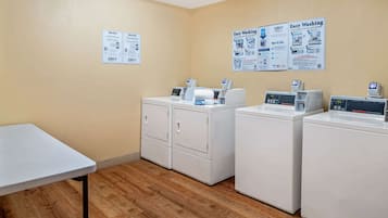 Een wasserij met drie wasmachines, een tafel en instructieposters aan de muur.