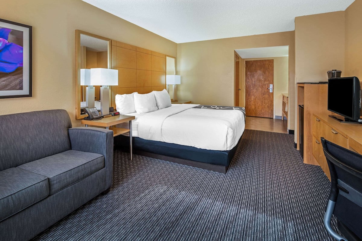 A hotel room with a bed, a desk with a lamp, a television, a sofa, and a mirror.
