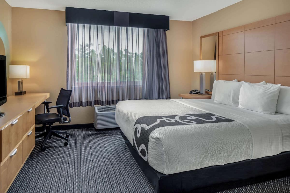 A hotel room with a large bed, a desk with a chair, a television, and a window with curtains.