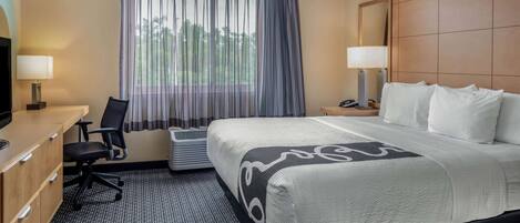 Una habitación de hotel con una cama grande, un escritorio con silla, un televisor y una ventana con cortinas.