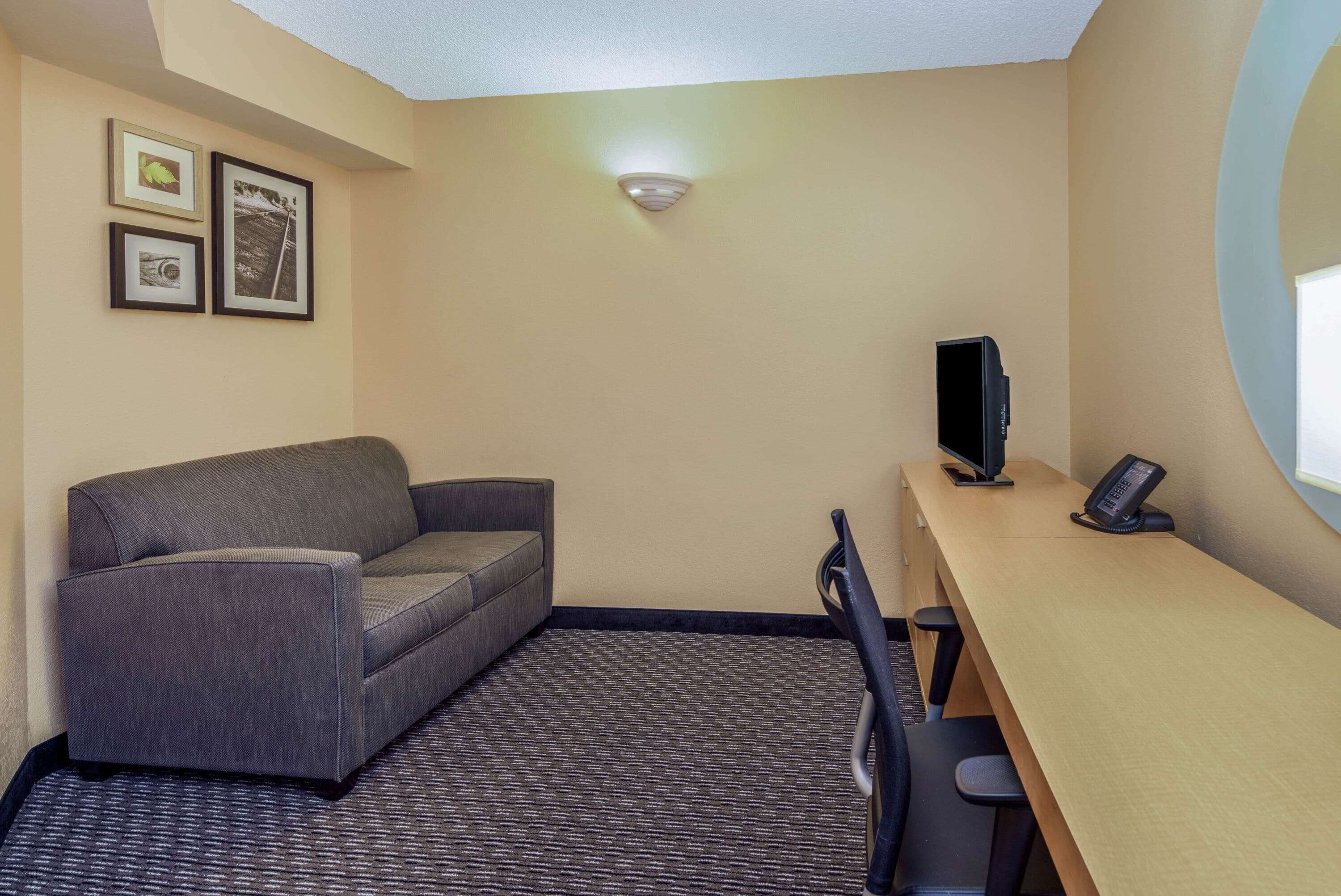 A hotel room with a sofa, a desk with a computer and phone, and framed pictures on the wall.
