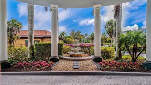 Un jardín techado con una fuente central, rodeado de palmeras y plantas con flores.
