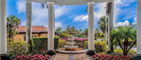 A covered garden area with a central fountain, surrounded by palm trees and flowering plants.