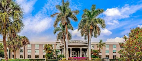Un hotel con un patio central, palmeras y un cielo azul despejado.