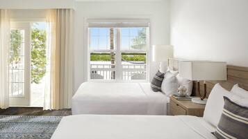 A hotel room with a large bed, a nightstand with a lamp, and a view of a white fence and greenery outside.
