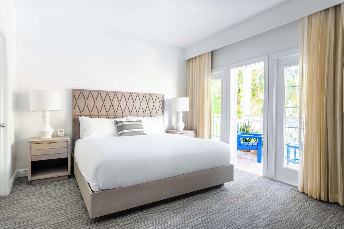 A hotel room with a large bed, two bedside tables with lamps, a wooden headboard, and a view of the outdoors through a sliding glass door.