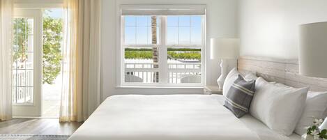 A hotel room with a large bed, a view of a white fence and greenery, and a balcony with a white railing.