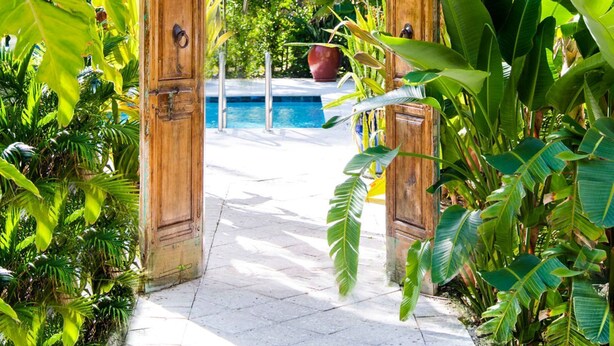 A wooden archway leading to a pool area surrounded by lush tropical vegetation. - Parrot Key Hotel & Villas (Key West)