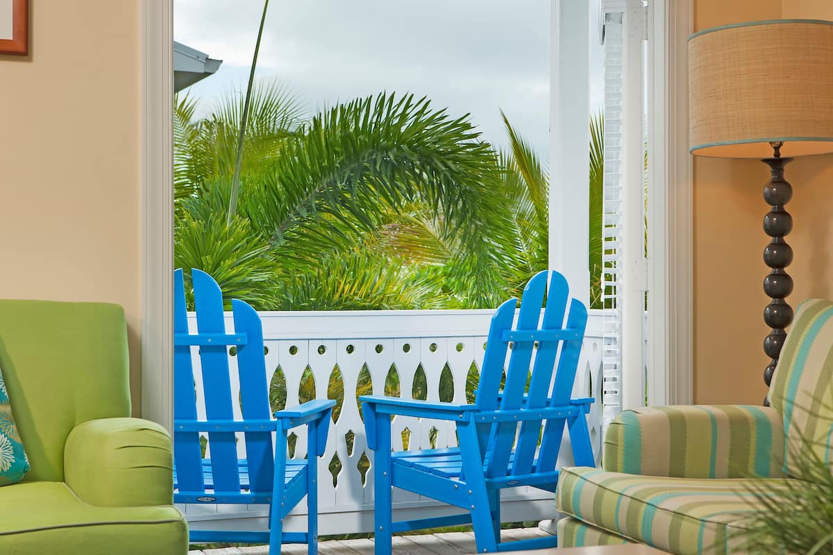 A room with a view of palm trees, two blue Adirondack chairs, a green sofa, and a striped armchair.