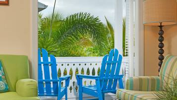 Una habitación con vistas a palmeras, dos sillas Adirondack azules, un sofá verde y un sillón a rayas.