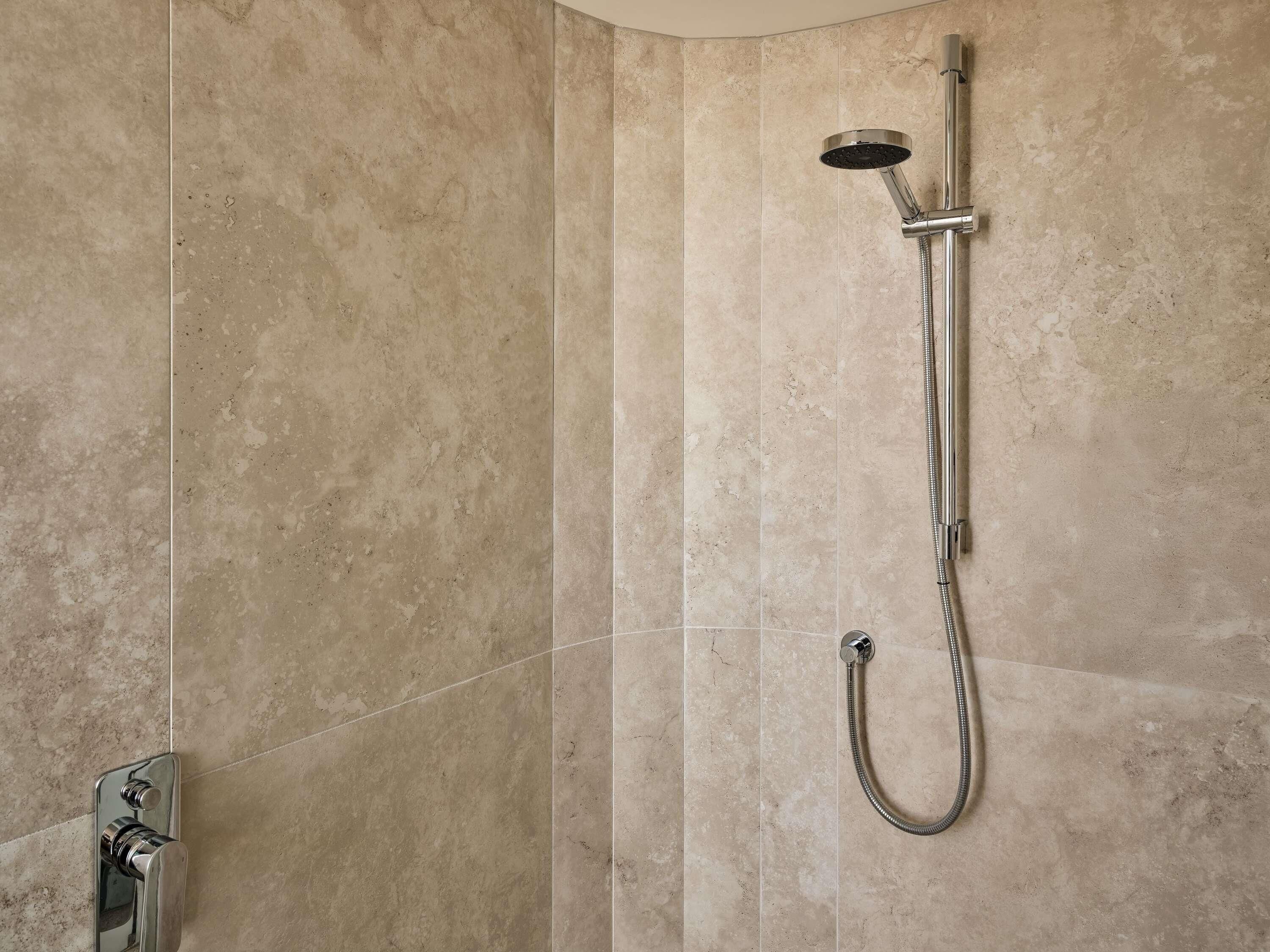 A shower with a handheld showerhead and a wall-mounted faucet in a bathroom with beige tiled walls.