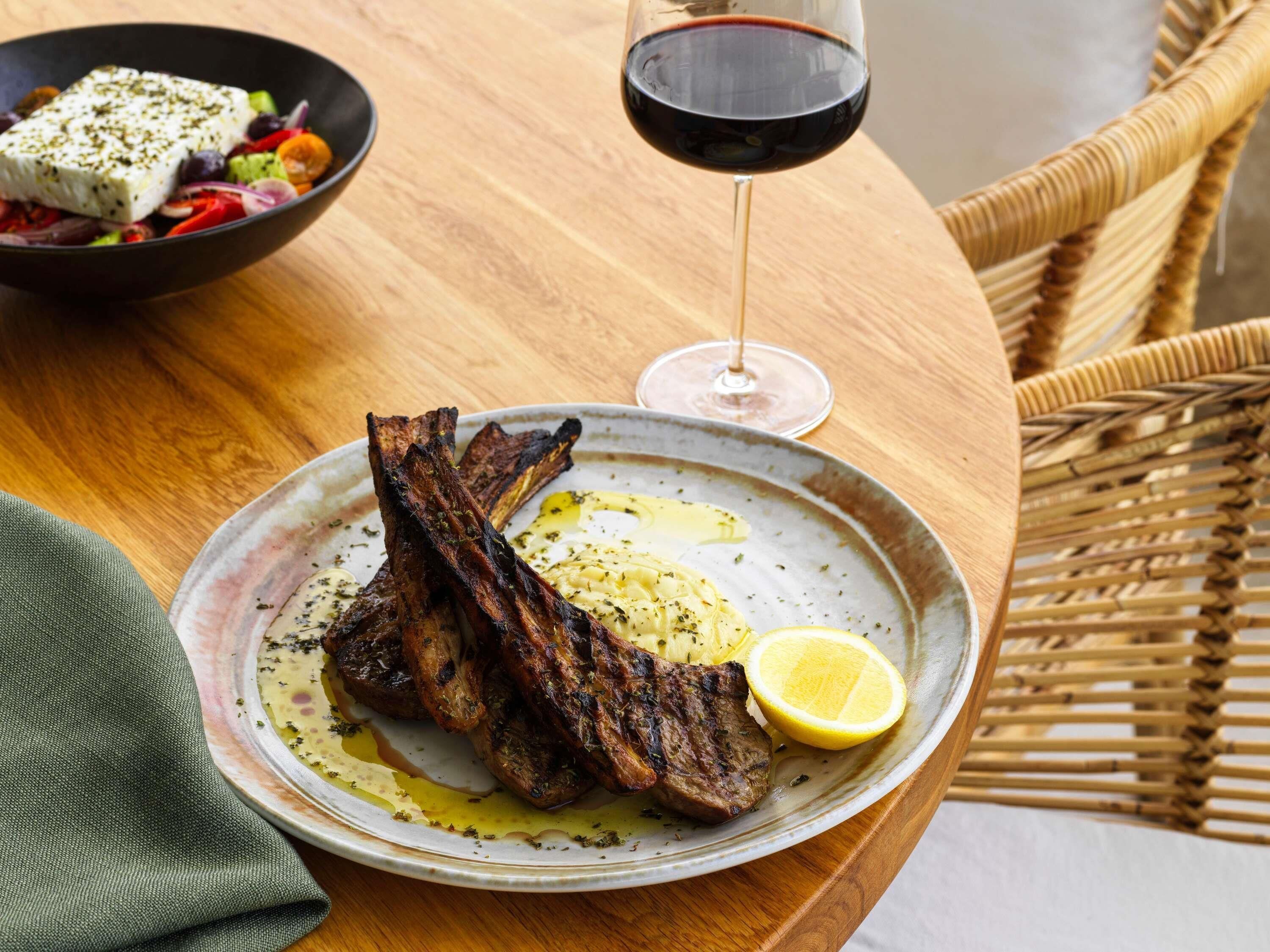 A plate with grilled meat, a lemon wedge, and a glass of red wine on a wooden table.
