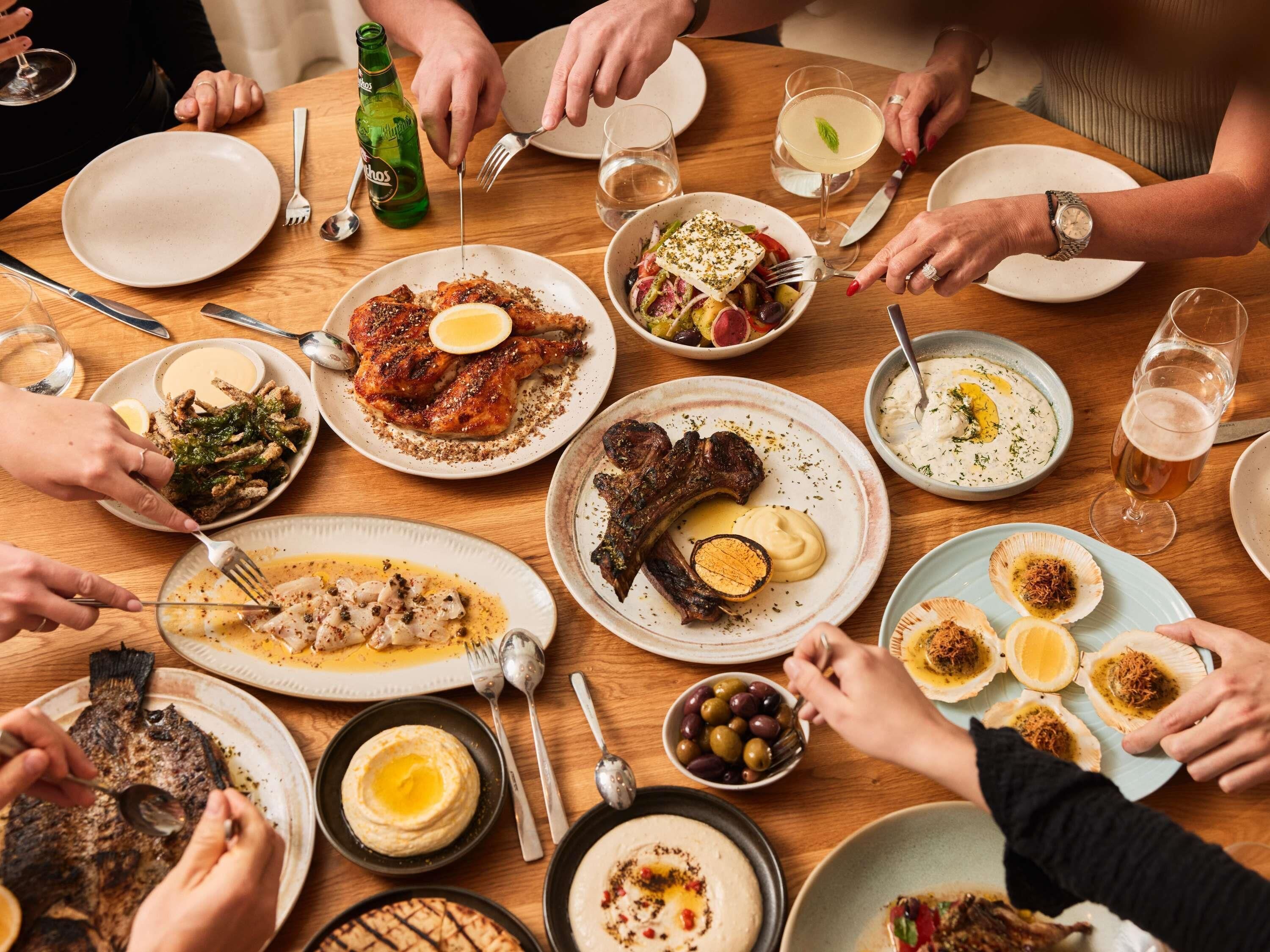 Un gruppo di persone cena attorno a un tavolo di legno, con diversi piatti e bevande.