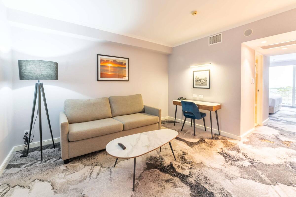 A modern living room with a sofa, a coffee table, a desk with a chair, a floor lamp, and framed pictures on the walls.