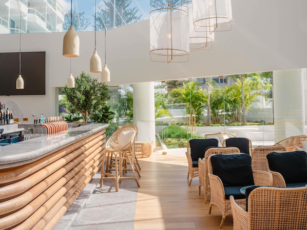 A modern bar area with a curved counter, wicker chairs, and hanging pendant lights.