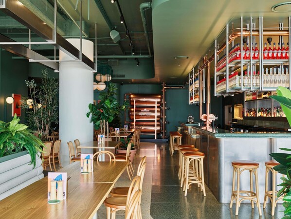 Uma área de bar moderna com banquetas de madeira, um balcão comprido e diversos frascos em prateleiras.