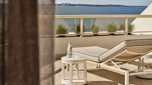 A balcony with a white lounge chair, a small round table, and a bottle of water. - The Brighton Hotel Sydney - MGallery Collection (Brighton-le-Sands)