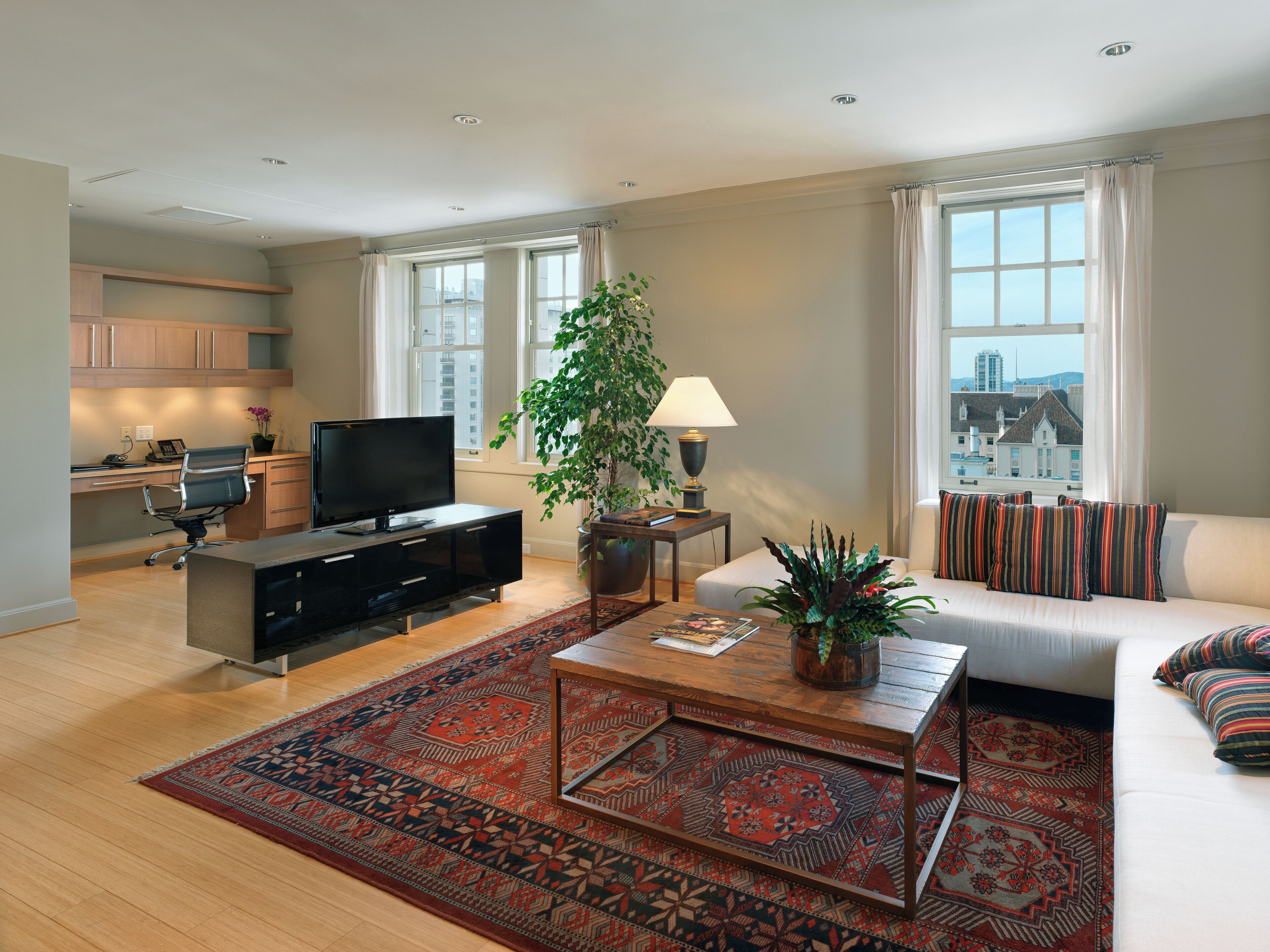 A modern living room with a flat-screen TV, a sofa, a coffee table, and a large window with curtains.