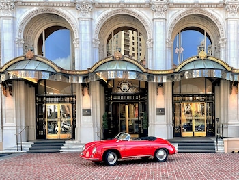 A maroon sports car parked in front of a grand hotel entrance with a brick facade and ornate detailing. at InterContinental Mark Hopkins by IHG